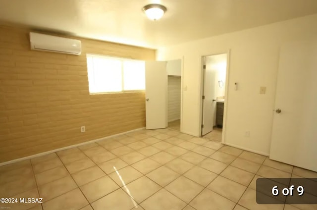 unfurnished bedroom featuring a wall mounted air conditioner, light tile patterned floors, connected bathroom, and brick wall