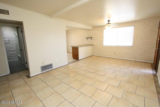 unfurnished room with beamed ceiling, light tile patterned flooring, ceiling fan, and brick wall