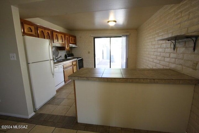 kitchen featuring tile counters, brick wall, kitchen peninsula, white appliances, and light tile patterned floors