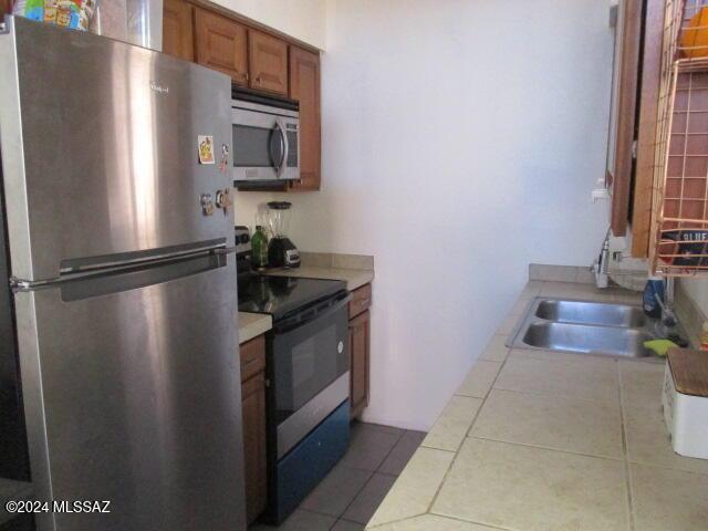 kitchen featuring sink, light tile patterned floors, tile counters, and appliances with stainless steel finishes