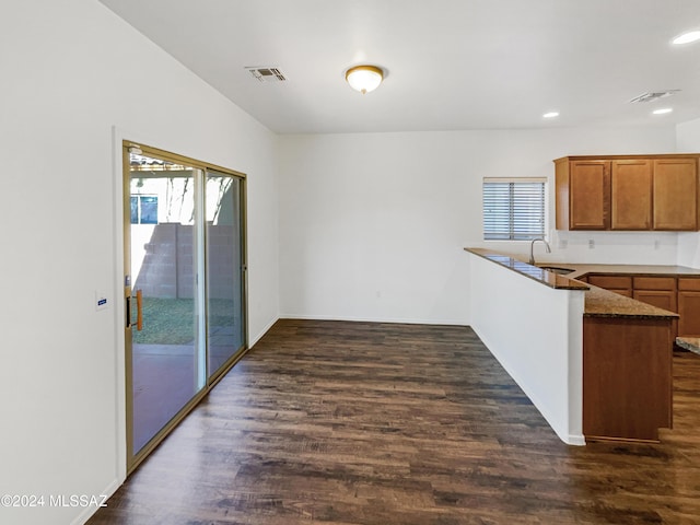 kitchen featuring kitchen peninsula, dark stone countertops, dark wood-type flooring, and sink