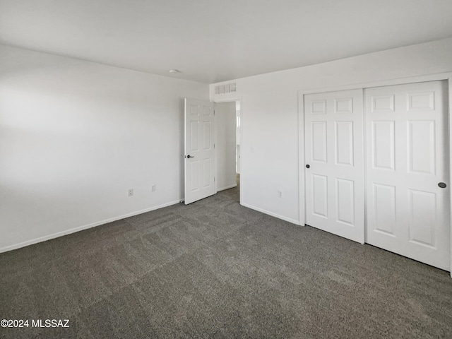 unfurnished bedroom with dark carpet and a closet