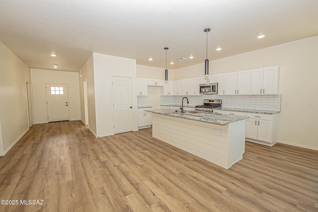 kitchen with appliances with stainless steel finishes, white cabinetry, hanging light fixtures, light stone counters, and a center island with sink