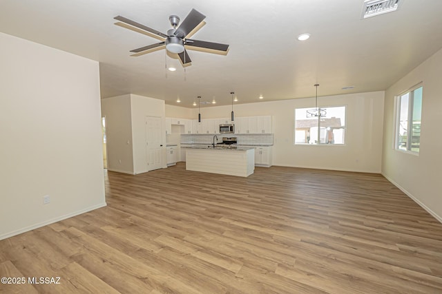 unfurnished living room with baseboards, visible vents, ceiling fan, a sink, and light wood-type flooring