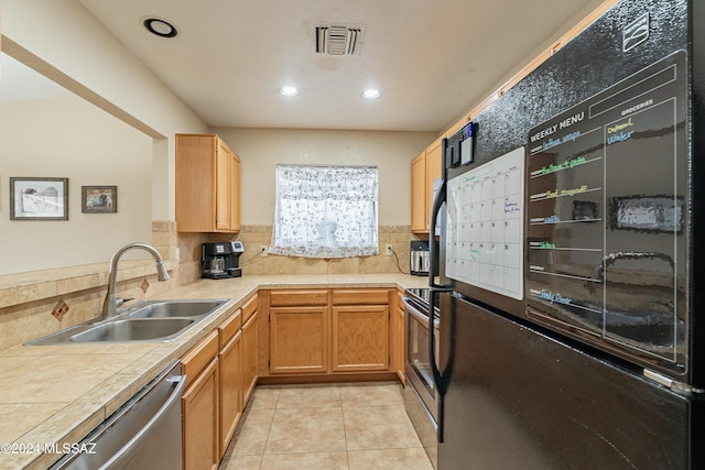 kitchen with appliances with stainless steel finishes, light tile patterned floors, tile counters, and sink