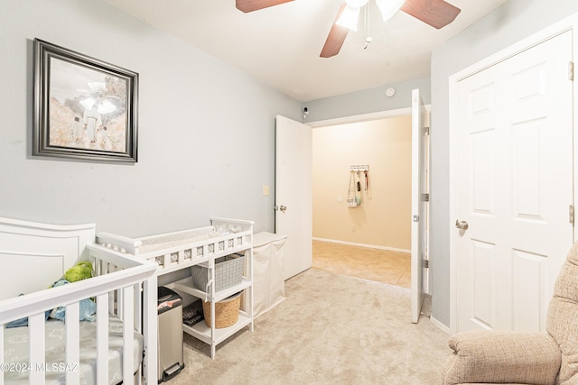 carpeted bedroom featuring ceiling fan and a crib