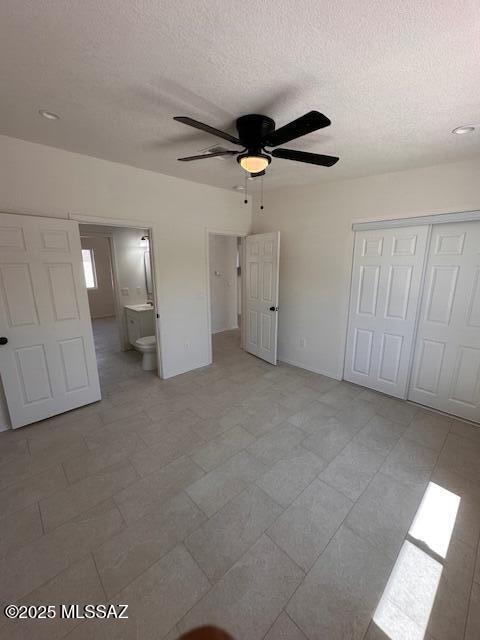 unfurnished bedroom featuring ensuite bath, a closet, ceiling fan, and a textured ceiling