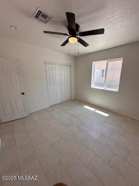 unfurnished bedroom featuring a textured ceiling, ceiling fan, light tile patterned floors, and a closet