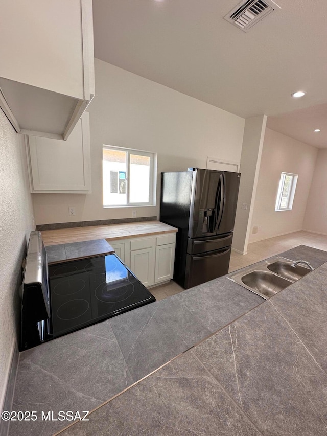 kitchen with fridge with ice dispenser, white cabinets, electric stove, and sink