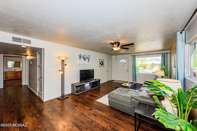 living room with a textured ceiling, ceiling fan, and dark wood-type flooring