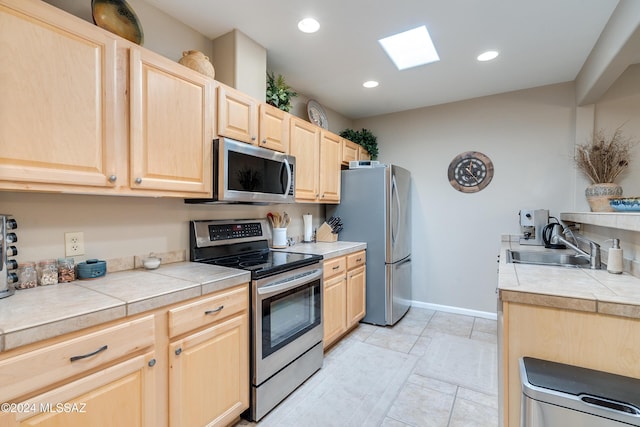 kitchen with appliances with stainless steel finishes, tile counters, sink, and light brown cabinets