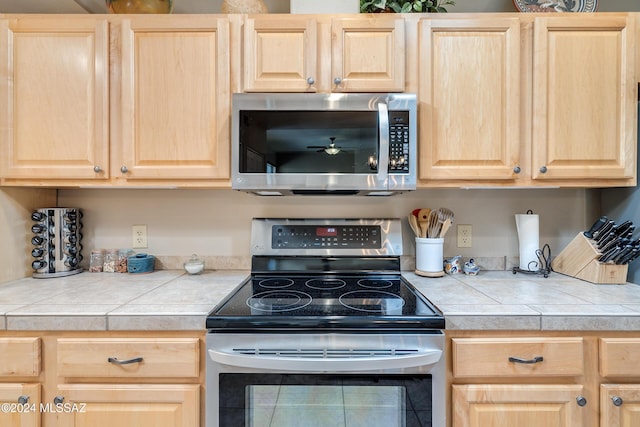 kitchen with appliances with stainless steel finishes, tile countertops, and light brown cabinets