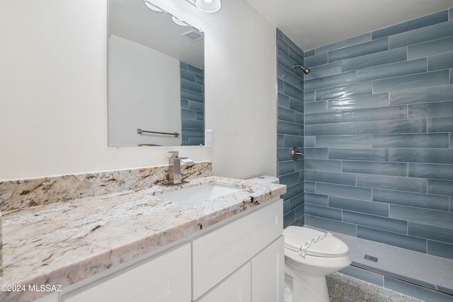 bathroom with a tile shower, vanity, and toilet