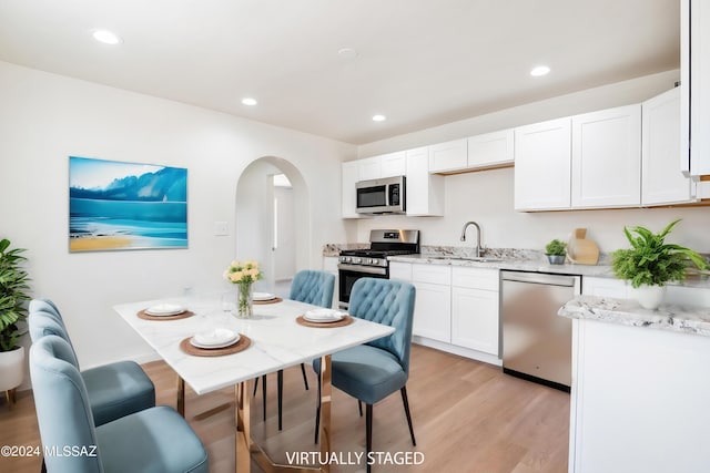 kitchen featuring light stone countertops, sink, stainless steel appliances, light hardwood / wood-style flooring, and white cabinets