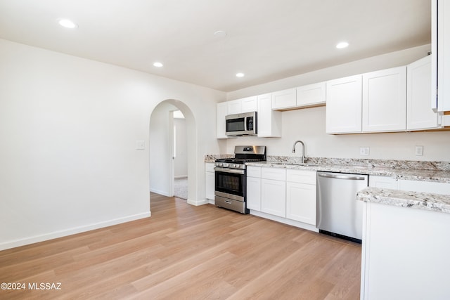 kitchen featuring light stone countertops, white cabinetry, sink, light hardwood / wood-style flooring, and appliances with stainless steel finishes