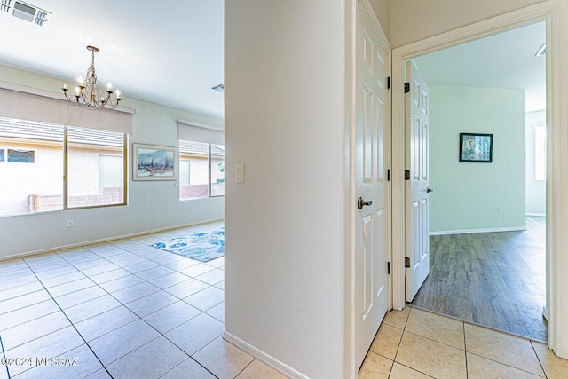 hall with light tile patterned floors and an inviting chandelier