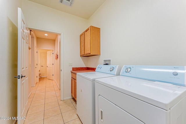 laundry area featuring washing machine and dryer, light tile patterned floors, and cabinets