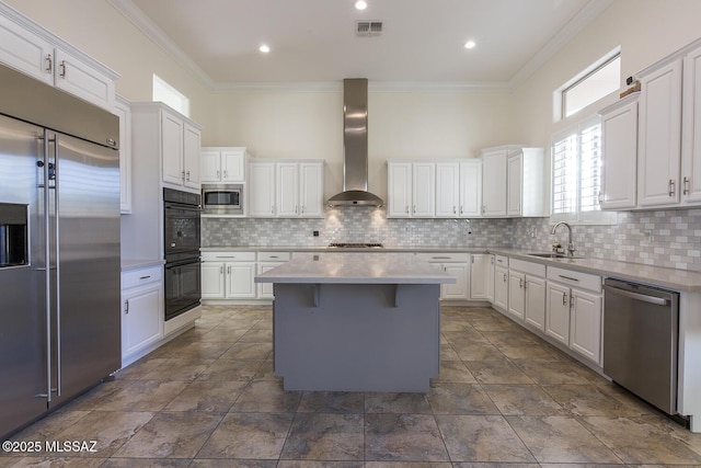 kitchen with backsplash, wall chimney range hood, built in appliances, white cabinets, and a kitchen island