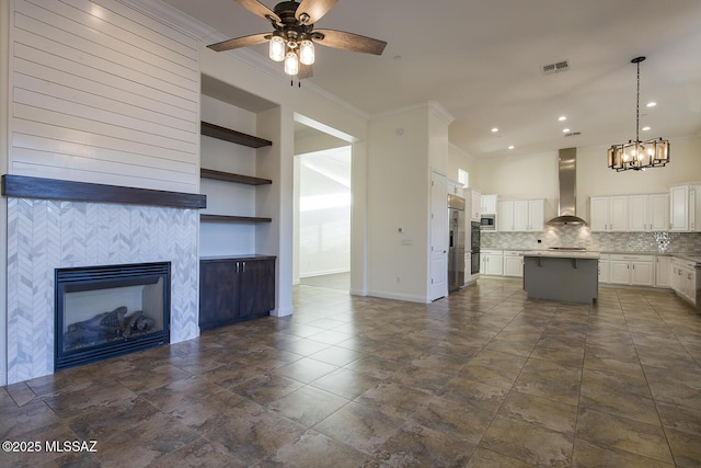 unfurnished living room featuring a tile fireplace, built in features, ceiling fan, and crown molding