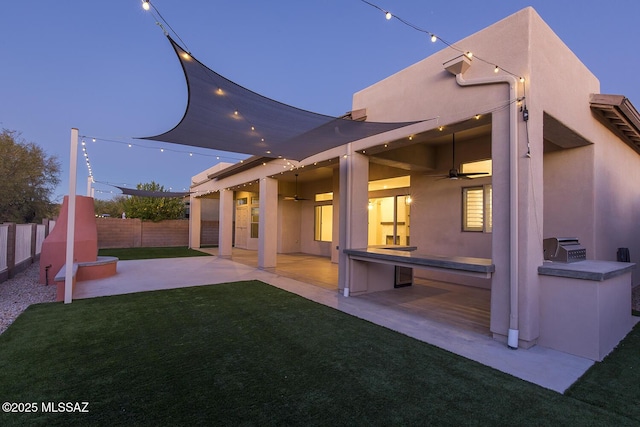 back house at dusk with a lawn, area for grilling, a patio area, and ceiling fan