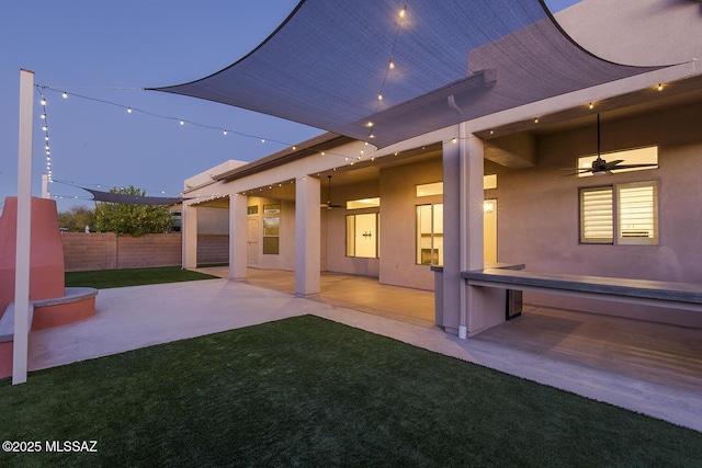 back house at dusk featuring a patio area, ceiling fan, and a yard