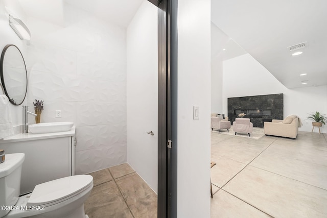 bathroom featuring vanity, tile patterned floors, toilet, a fireplace, and tile walls