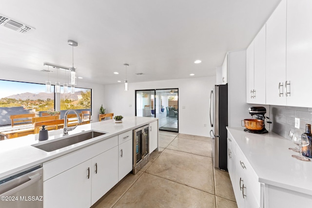 kitchen featuring white cabinets, sink, wine cooler, appliances with stainless steel finishes, and decorative light fixtures