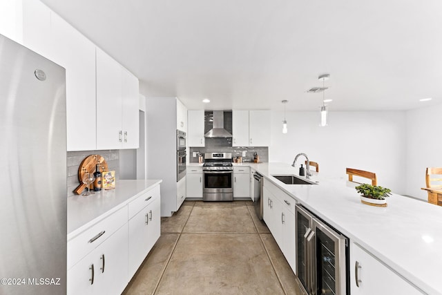 kitchen featuring white cabinetry, sink, wall chimney exhaust hood, pendant lighting, and appliances with stainless steel finishes