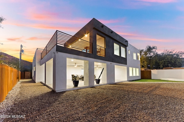 property exterior at dusk with ceiling fan, a balcony, and a patio