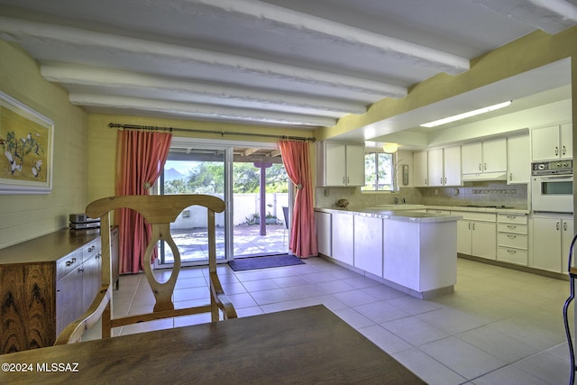 kitchen featuring beamed ceiling, oven, white cabinetry, and tasteful backsplash