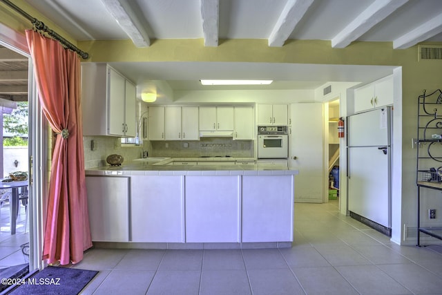 kitchen featuring tile countertops, white appliances, backsplash, beam ceiling, and white cabinetry