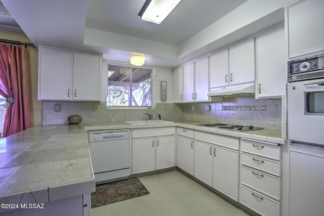 kitchen with tile countertops, white appliances, backsplash, sink, and white cabinetry