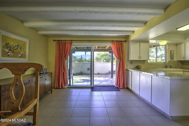 kitchen with decorative backsplash, white cabinetry, beamed ceiling, and light tile patterned floors