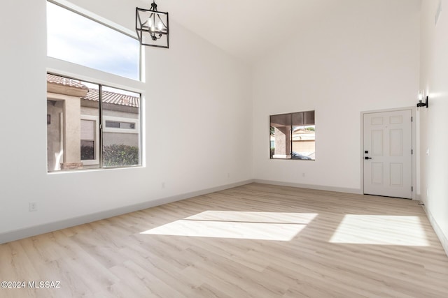 spare room featuring a notable chandelier, light hardwood / wood-style floors, and high vaulted ceiling