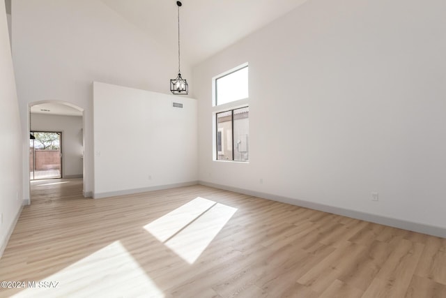 spare room with a notable chandelier, light wood-type flooring, and a towering ceiling