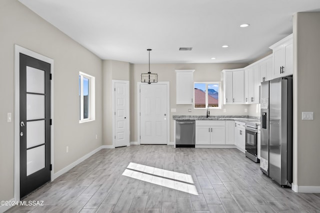 kitchen featuring light wood-type flooring, light stone counters, stainless steel appliances, decorative light fixtures, and white cabinetry