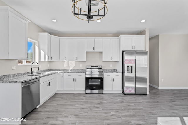 kitchen featuring light stone counters, stainless steel appliances, sink, a notable chandelier, and white cabinetry