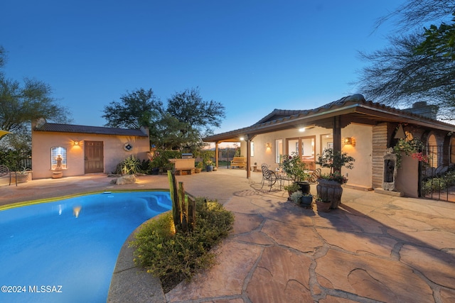 pool at dusk with a patio area and an outbuilding