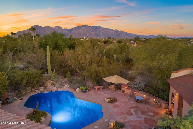 pool at dusk featuring a mountain view and a patio