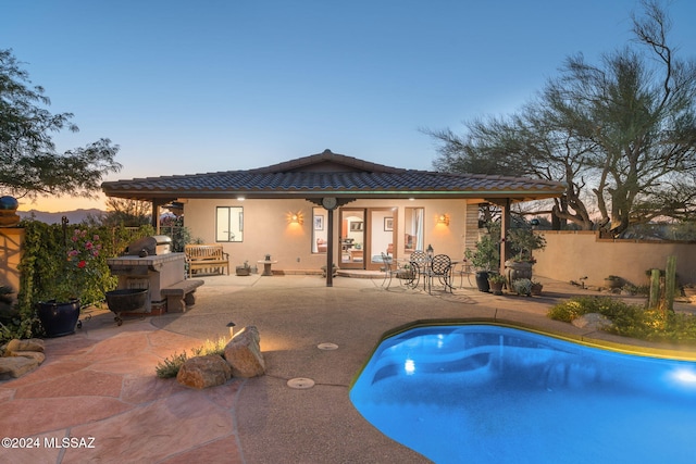 pool at dusk with a patio and exterior fireplace