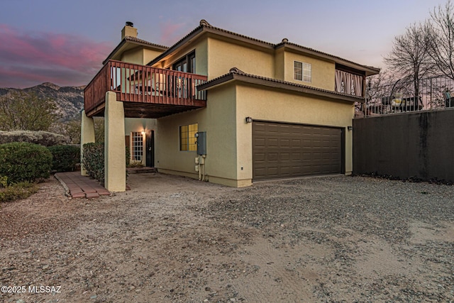 back house at dusk with a garage and a deck with mountain view