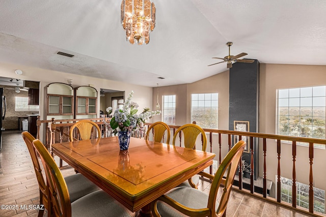 dining room featuring lofted ceiling, ceiling fan with notable chandelier, a textured ceiling, and light hardwood / wood-style flooring