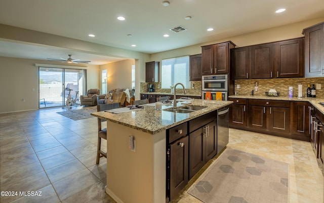 kitchen featuring ceiling fan, sink, light stone countertops, a kitchen bar, and a center island with sink