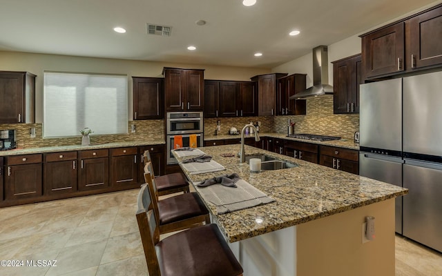 kitchen featuring appliances with stainless steel finishes, sink, a kitchen island with sink, and wall chimney range hood