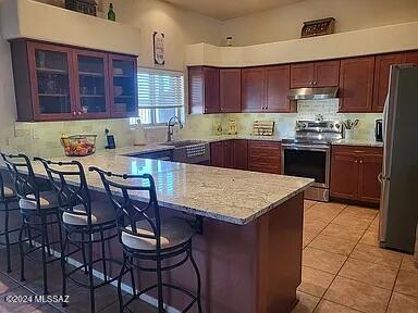 kitchen with kitchen peninsula, appliances with stainless steel finishes, decorative backsplash, light tile patterned floors, and a breakfast bar area