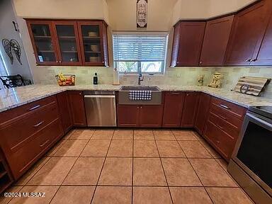 kitchen with decorative backsplash, appliances with stainless steel finishes, light stone counters, sink, and light tile patterned floors