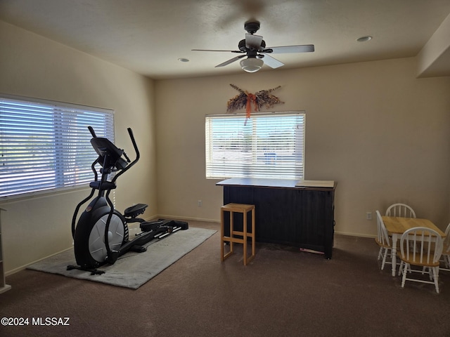 exercise room with dark colored carpet, ceiling fan, and a healthy amount of sunlight