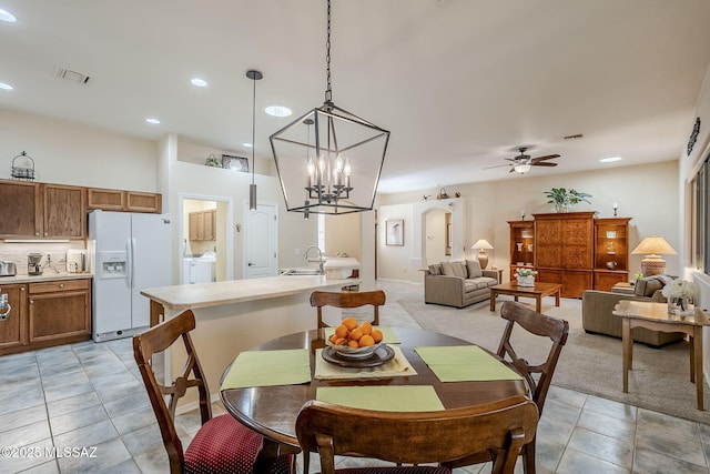 dining space with washer / clothes dryer, light tile patterned flooring, sink, and ceiling fan with notable chandelier