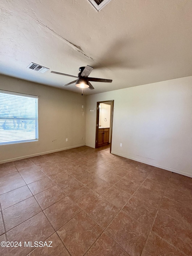 tiled empty room with ceiling fan and a textured ceiling