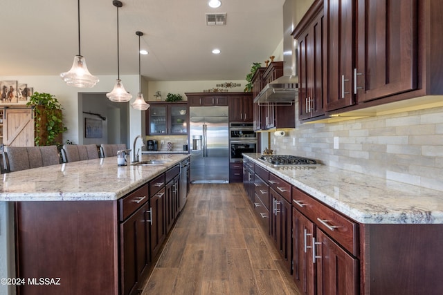 kitchen with dark wood-type flooring, a large island with sink, sink, hanging light fixtures, and appliances with stainless steel finishes